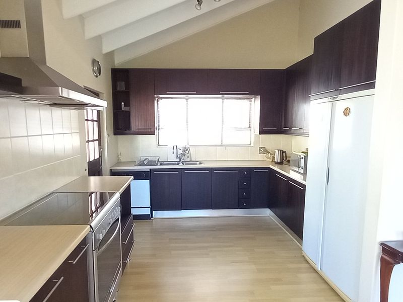 A functional kitchen featuring dark wood cabinetry, laminate countertops, a built-in oven with hob, and a vaulted ceiling providing a spacious feel.