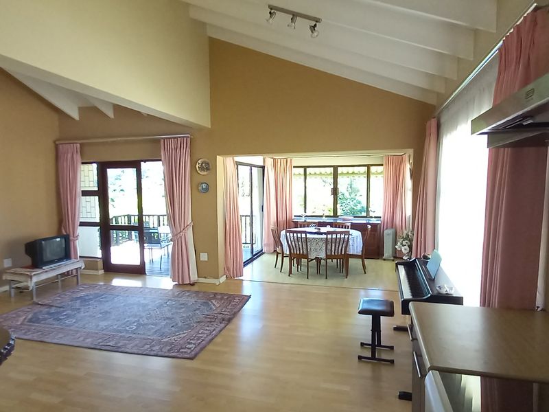 Spacious open-plan living and dining area featuring vaulted ceilings with exposed beams, laminate flooring, and direct access to an outdoor patio through sliding doors.
