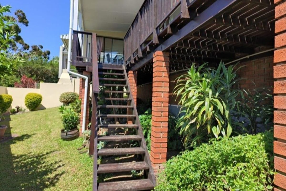 Rear exterior view of the townhouse featuring a raised timber deck, wooden staircase, and brick support columns overlooking the garden area.