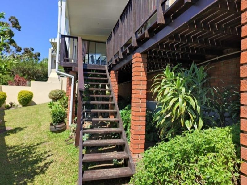 Rear exterior view of the townhouse featuring a raised timber deck, wooden staircase, and brick support columns overlooking the garden area.