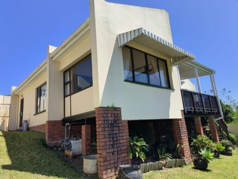 Rear elevation of the townhouse featuring a raised timber deck, brick foundation piers, and metal window awnings set against a landscaped garden.