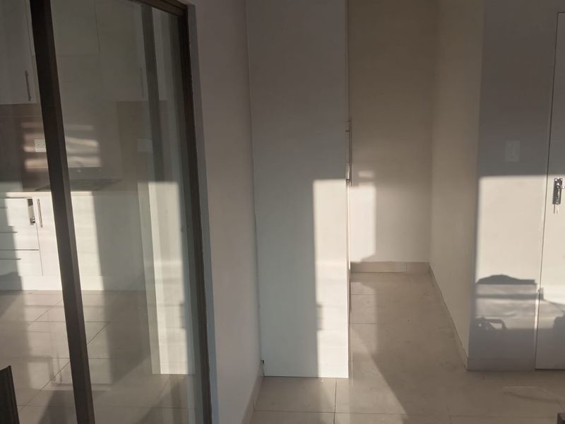 A bright, empty hallway featuring tiled flooring, built-in cabinetry, and a glass sliding door leading to an adjacent room.