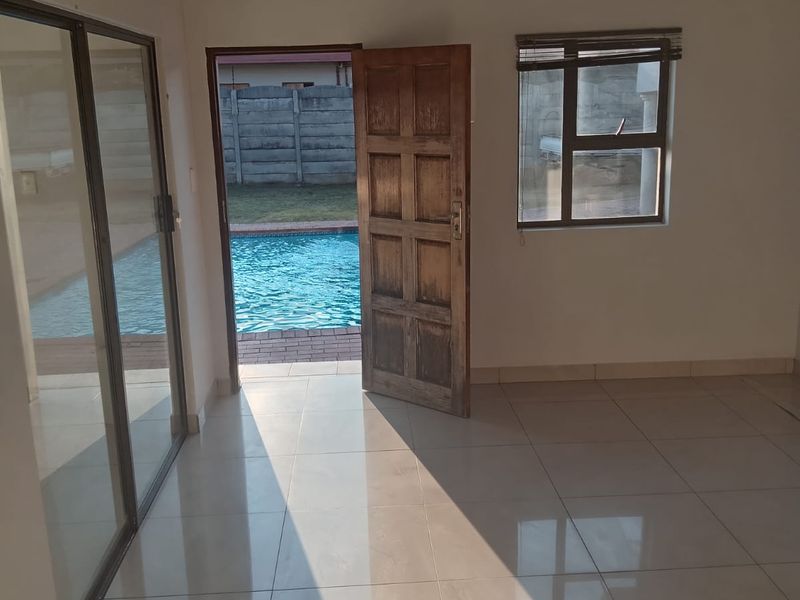 Bright, empty living area featuring tiled floors, recessed lighting, and direct access to an outdoor pool area through a sliding glass door.