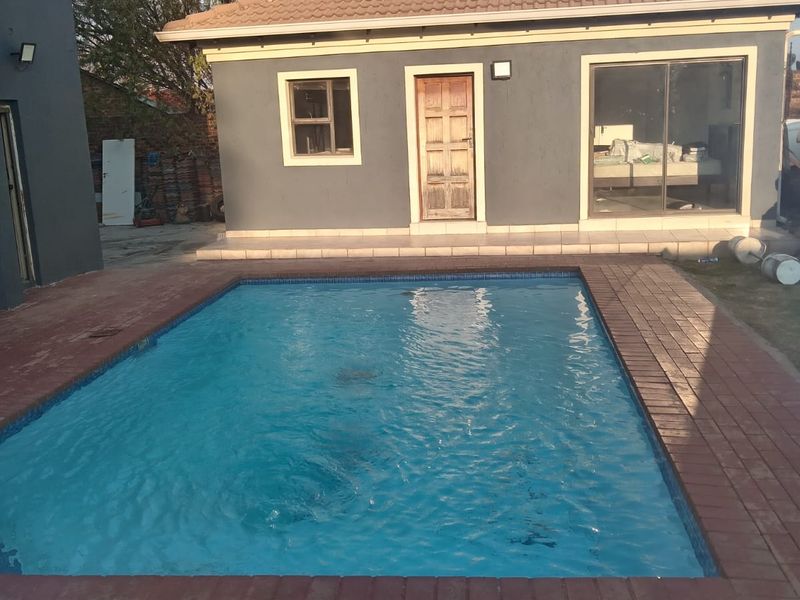 Outdoor pool area featuring a rectangular swimming pool surrounded by brick paving, adjacent to a detached cottage structure with a tiled roof.