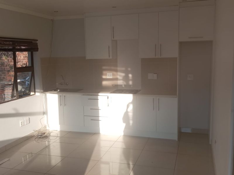 A clean, modern kitchen featuring white built-in cabinetry, tiled flooring, and a tiled splashback, offering a bright and functional workspace.