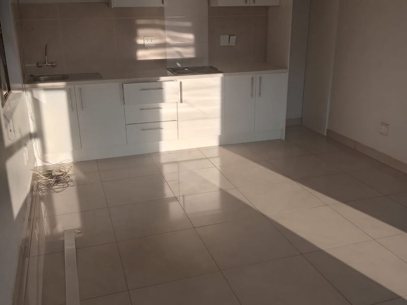 A clean, empty kitchen featuring white built-in cabinetry, tiled flooring, a stainless steel sink, and a built-in hob, ready for personalization.