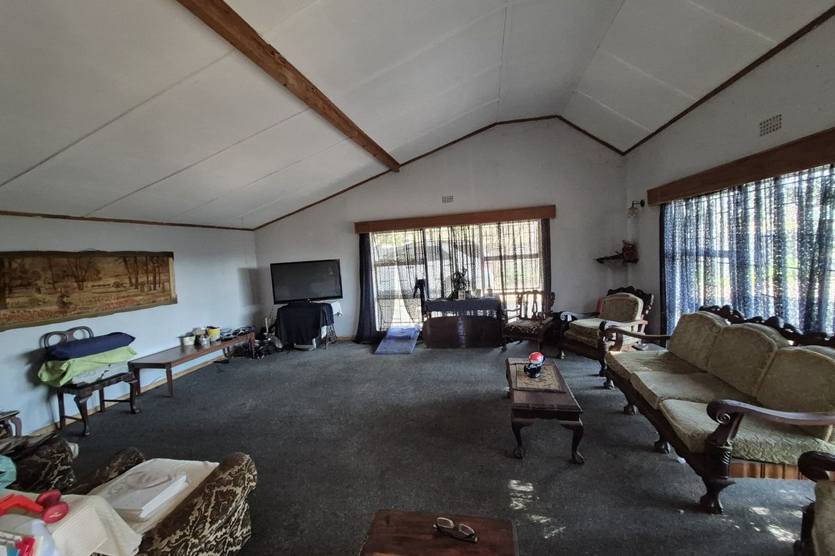 Spacious living room featuring a vaulted ceiling with exposed timber beams and large windows, offering a dated interior ready for modernization.