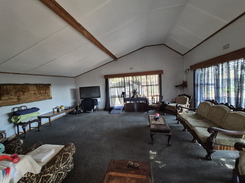 Spacious living room featuring a vaulted ceiling with exposed timber beams and large windows, offering a dated interior ready for modernization.