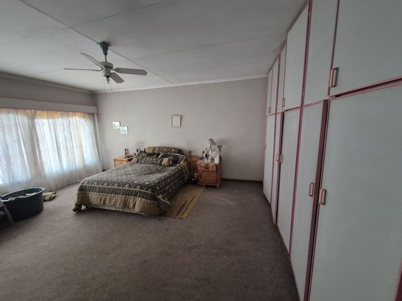 Spacious bedroom featuring extensive built-in cupboards and a ceiling fan, offering a functional layout with potential for modern updates.