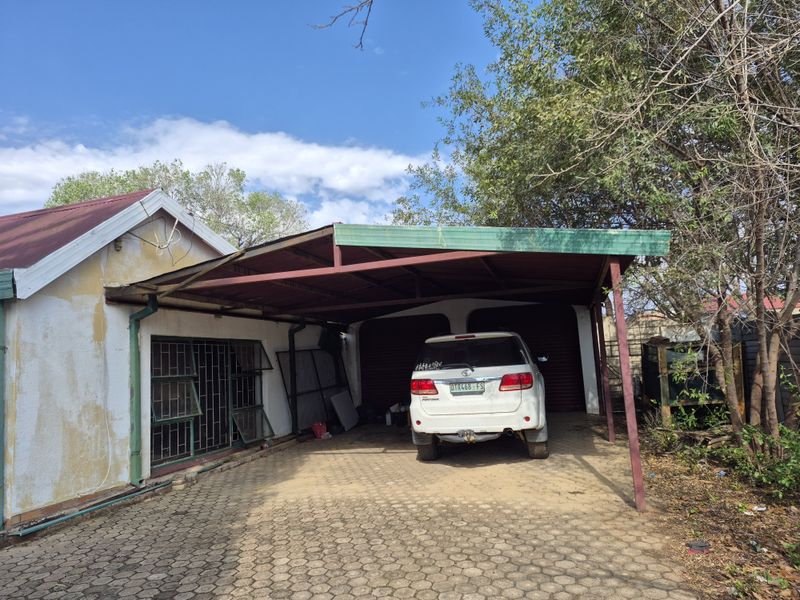 A detached carport structure with a paved driveway and roller shutter garage doors, showing signs of exterior wear and weathering.
