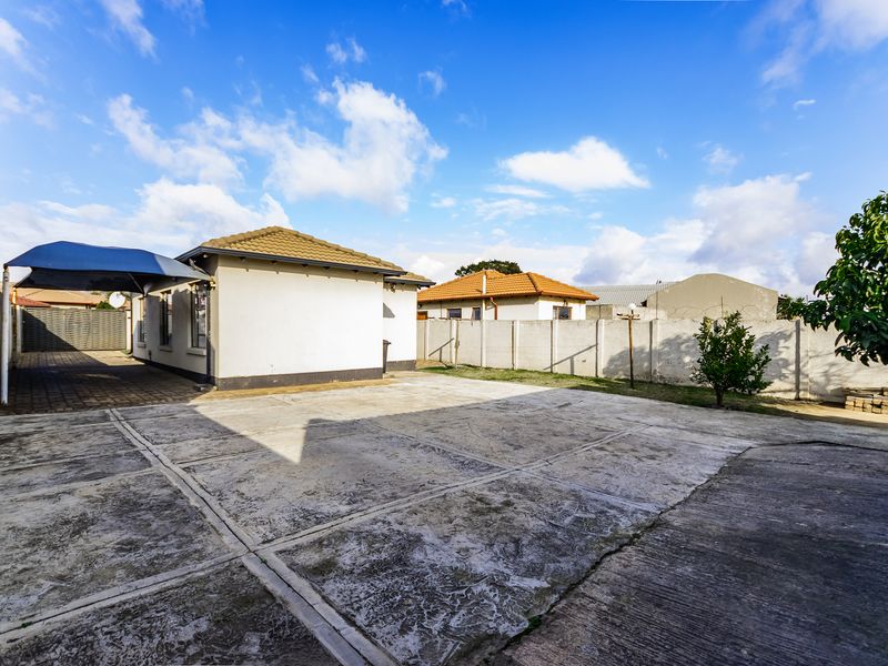 Spacious rear yard featuring extensive concrete paving, a covered carport, and secure precast concrete boundary walls.