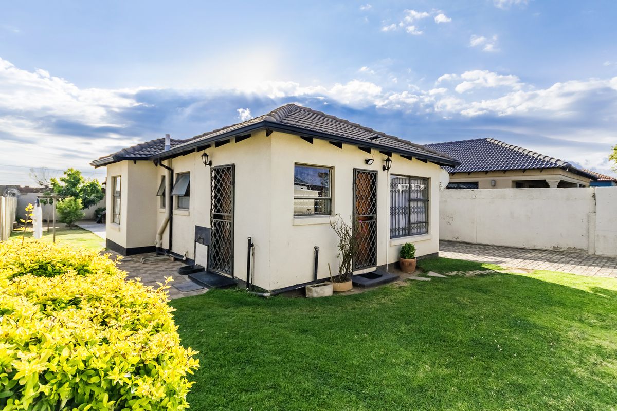 Rear view of the house featuring a tiled roof, security gates, and a well-maintained garden area with paved pathways.