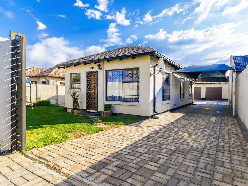 Front view of a well-maintained house featuring a paved driveway, carport, security gates, and a neat garden area.