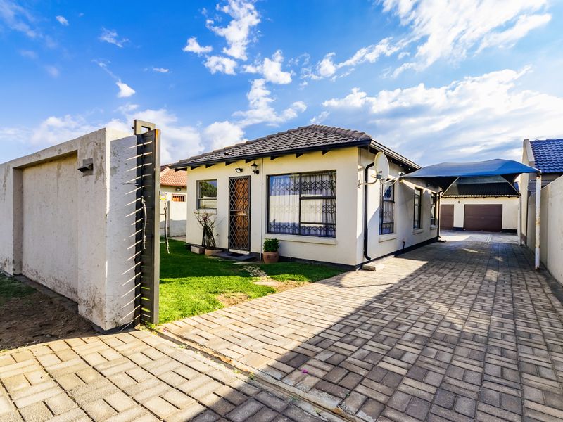 Front view of a detached house featuring a paved driveway, carport, security gate, and perimeter wall with a small front garden.