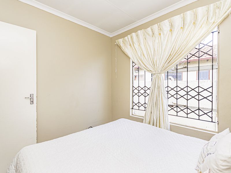 A functional bedroom featuring neutral wall tones and a window fitted with a security gate.