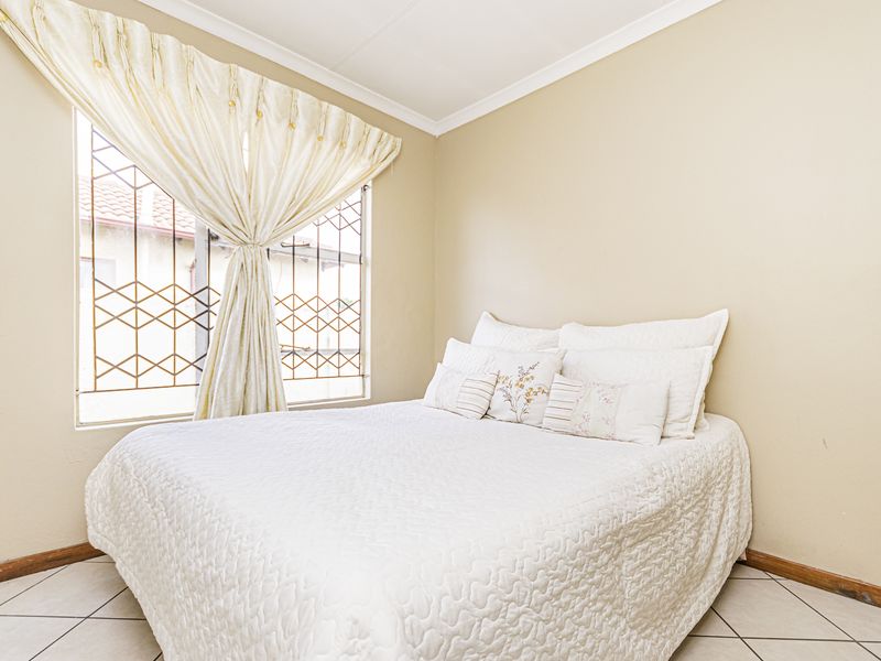 A standard bedroom featuring tiled flooring, neutral wall finishes, and a window fitted with a security gate.