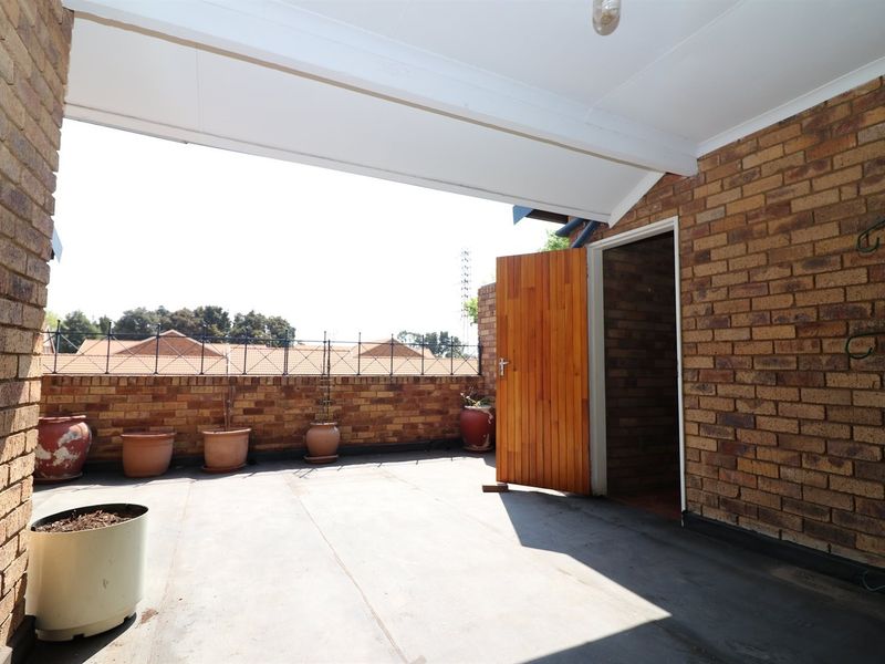 A covered outdoor patio area featuring exposed brick walls, concrete flooring, and a timber door leading into the property.
