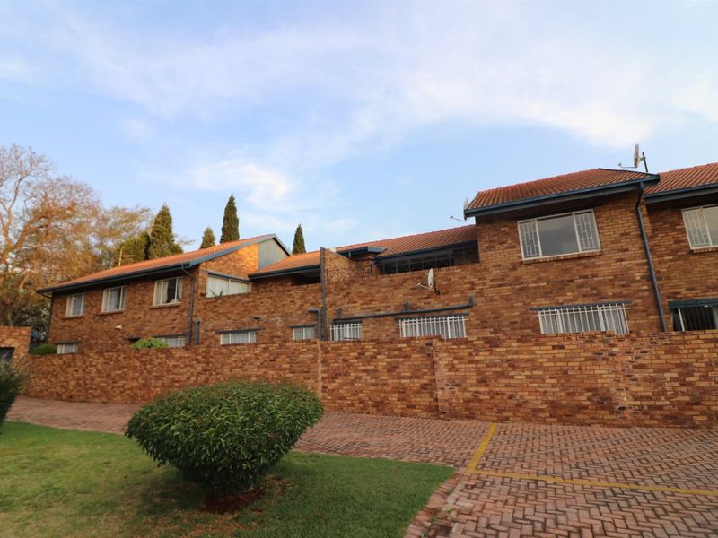 Front elevation of a multi-story face-brick townhouse complex featuring a paved driveway, tiled roofing, and security bars on windows.