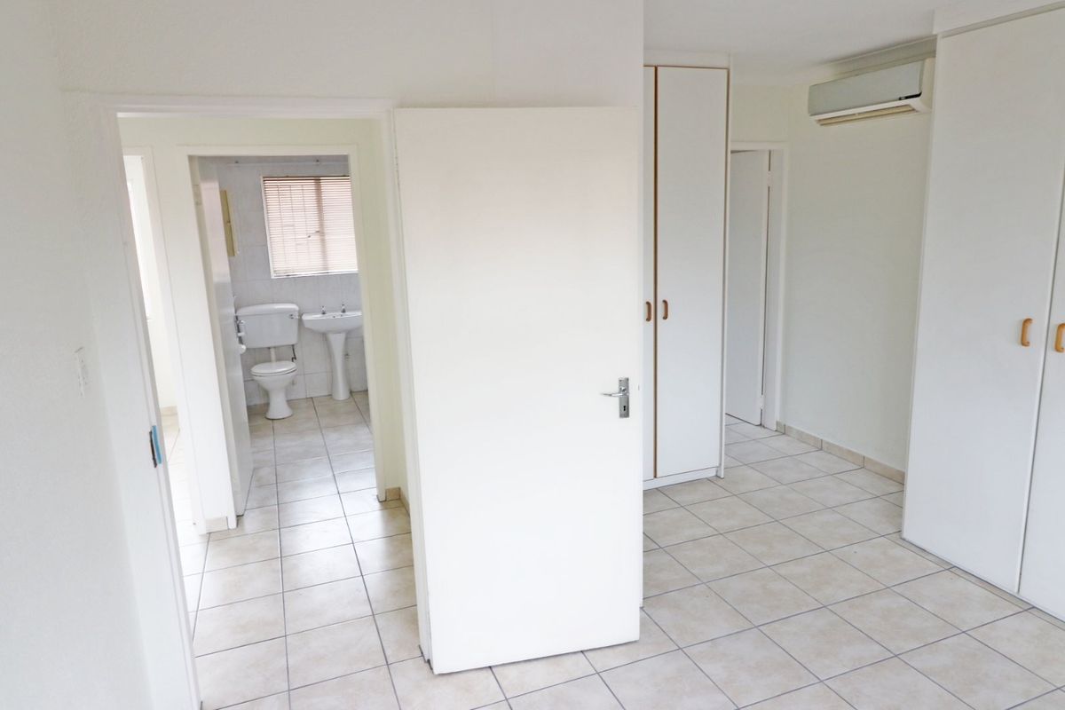 A bright, empty bedroom featuring tiled flooring, built-in cupboards, a wall-mounted air conditioner, and direct access to an en-suite bathroom.