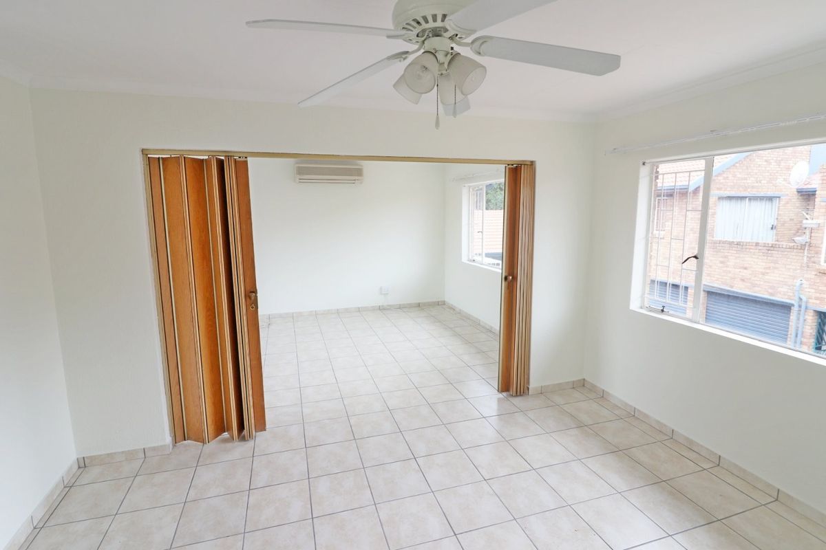 An empty living area featuring tiled flooring, a ceiling fan, a split-system air conditioner, and a folding door partition leading to an adjacent room.