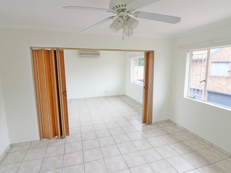 An empty living area featuring tiled flooring, a ceiling fan, a split-system air conditioner, and a folding door partition leading to an adjacent room.