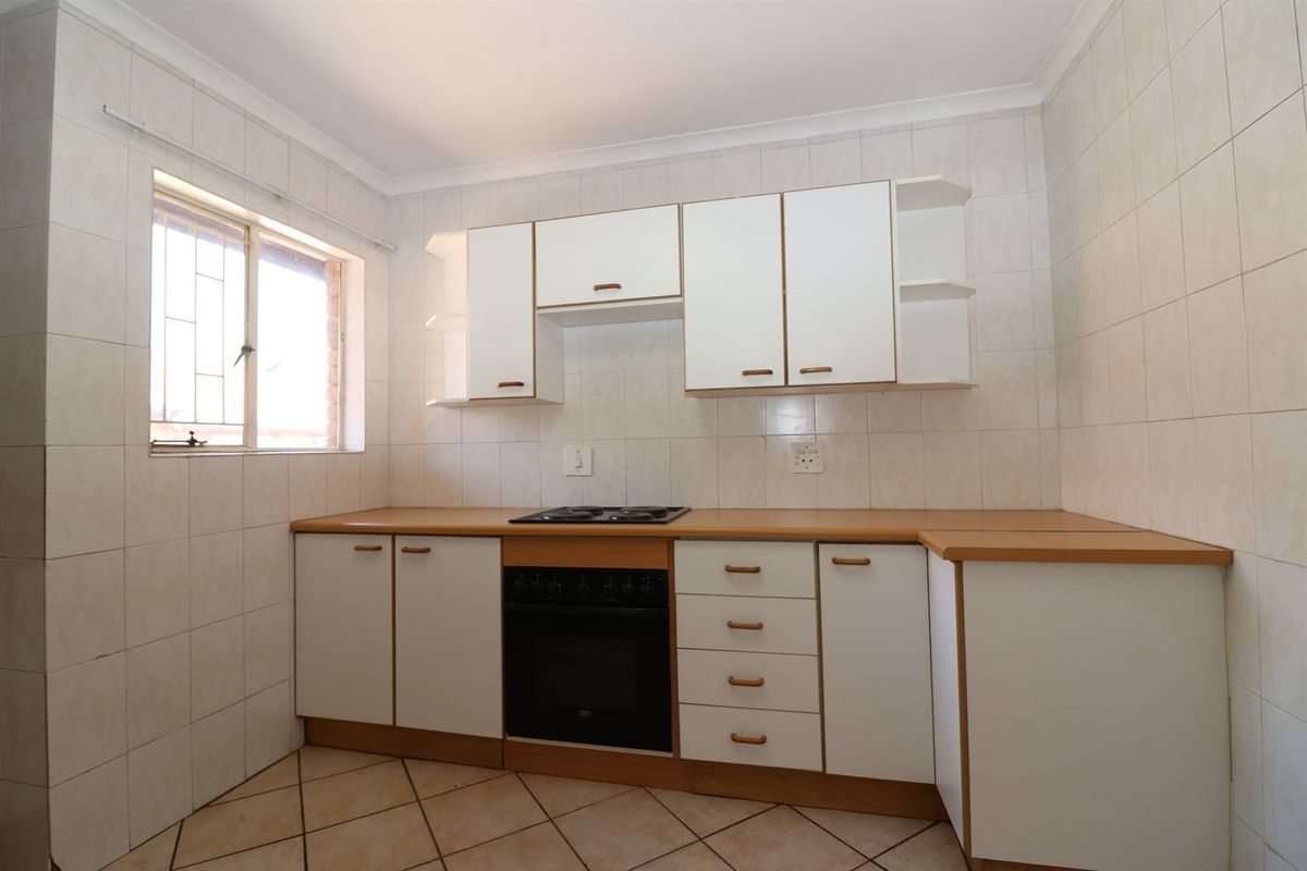 A functional kitchen featuring built-in cabinetry, laminate countertops, an integrated oven and hob, and fully tiled walls and floors.