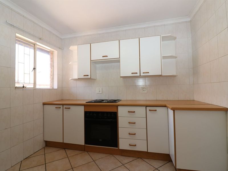 A functional kitchen featuring built-in cabinetry, laminate countertops, an integrated oven and hob, and fully tiled walls and floors.