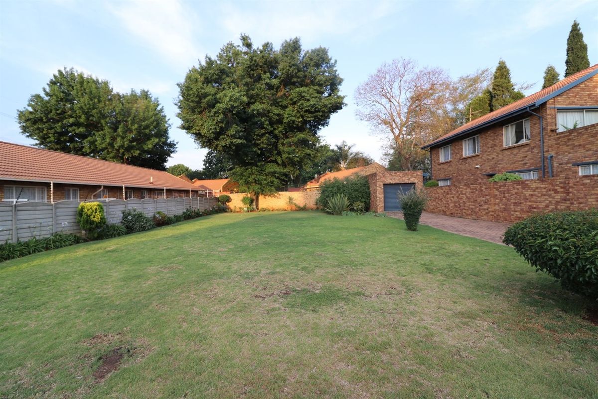 Spacious rear garden area featuring a large lawn, brick boundary walls, paved driveway access, and a single garage.
