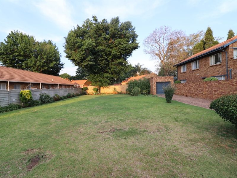 Spacious rear garden area featuring a large lawn, brick boundary walls, paved driveway access, and a single garage.