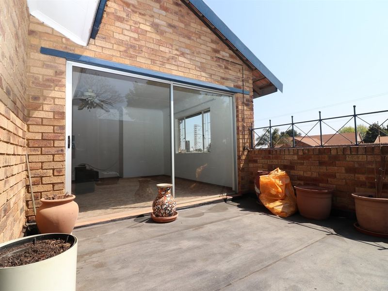 A private outdoor patio area featuring brick walls, a sliding glass door entrance, and metal perimeter railing, offering a functional space for outdoor living.