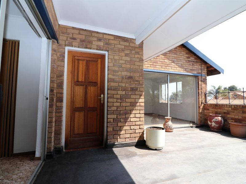 A covered outdoor patio area featuring exposed brick walls, sliding glass door access, and a metal safety railing.