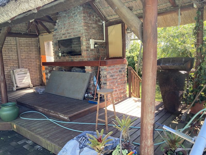 Covered outdoor patio area featuring a brick fireplace, built-in braai, and timber decking under a traditional thatched roof structure.