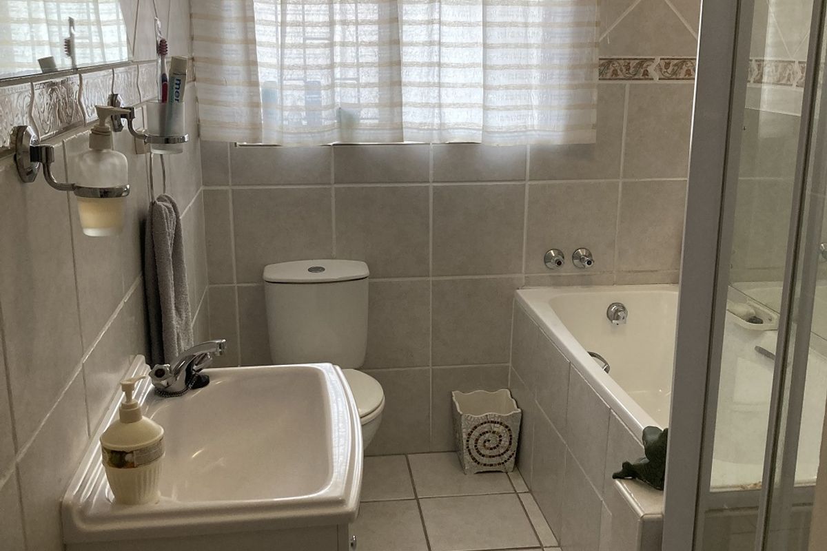 A functional bathroom featuring a vanity basin, toilet, bathtub, and separate shower enclosure with neutral wall and floor tiling.