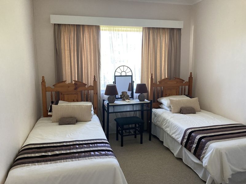 A functional bedroom featuring neutral wall tones, carpeted flooring, and a window with a built-in curtain pelmet.
