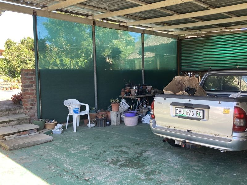 A covered outdoor parking area featuring a corrugated metal roof, concrete flooring, and brick retaining wall with shade cloth screening.