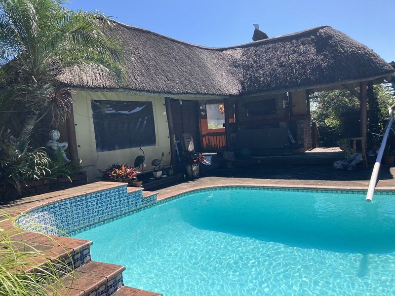 Outdoor pool area featuring a swimming pool with tiled coping, adjacent timber decking, and a covered entertainment space with a traditional thatched roof.