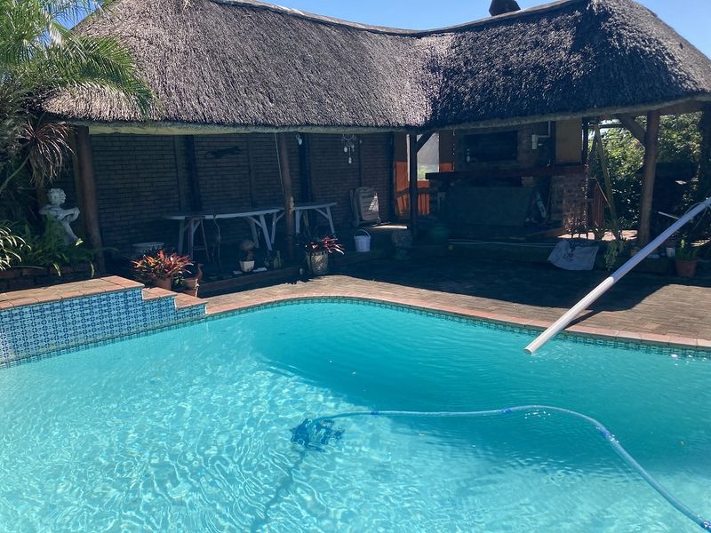 Outdoor entertainment area featuring a swimming pool and a covered patio with a thatched roof and built-in braai facility.