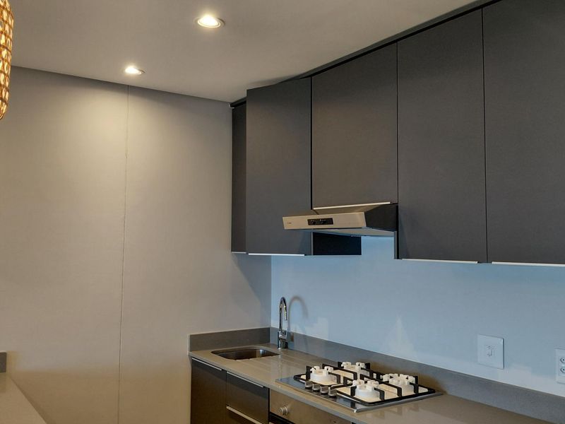 Modern kitchen featuring dark matte cabinetry, stone countertops, integrated gas hob, extractor fan, and stainless steel sink with recessed lighting.