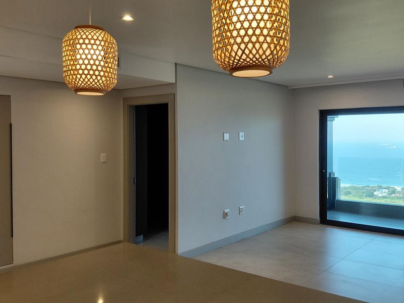 Spacious open-plan living area featuring modern tiled floors, recessed lighting, and a large sliding door leading to a balcony with ocean views.