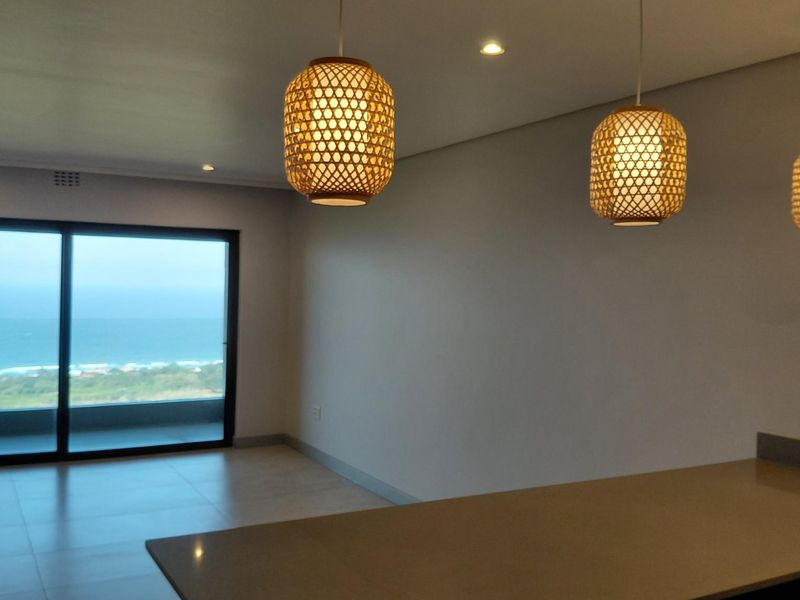 An open-plan living area featuring tiled floors, recessed lighting, and a large sliding glass door offering expansive ocean views.