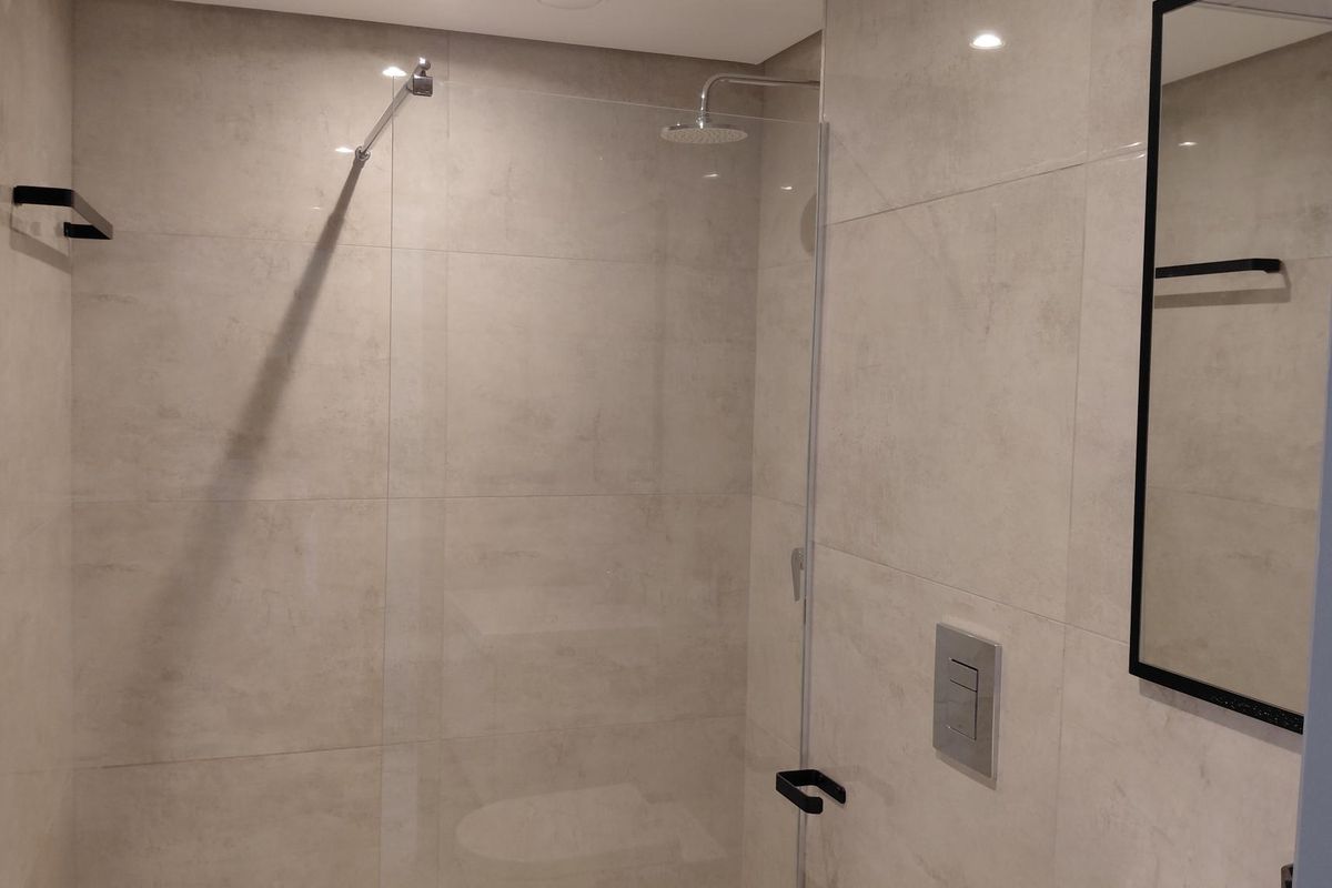 Modern bathroom featuring a walk-in shower with a glass screen, rain shower head, and contemporary black fixtures against neutral tiled walls.