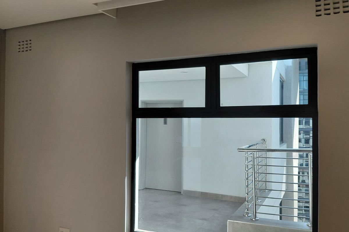 A bright, empty bedroom featuring modern aluminium window frames and direct access to an external balcony area.
