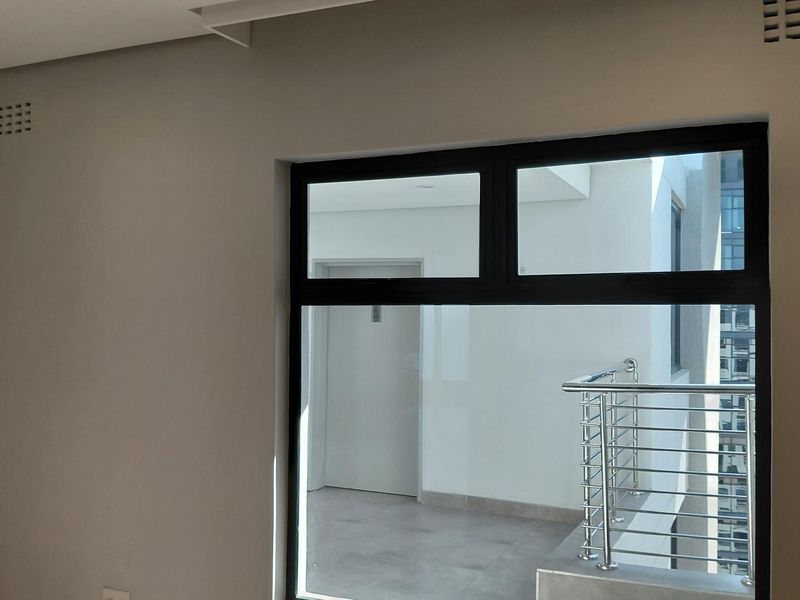 A bright, empty bedroom featuring modern aluminium window frames and direct access to an external balcony area.