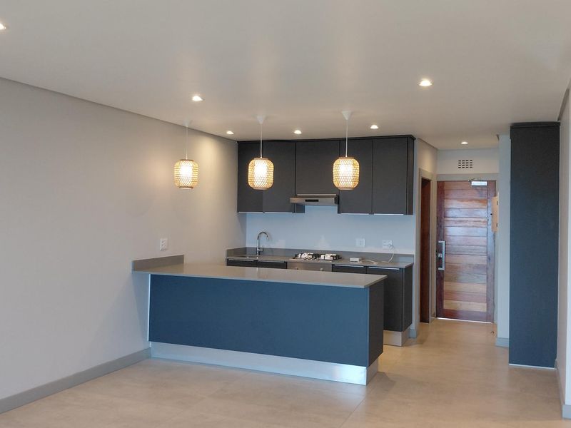 Modern open-plan kitchen featuring dark cabinetry, stone countertops, integrated hob, and recessed lighting, seamlessly flowing into the living area.