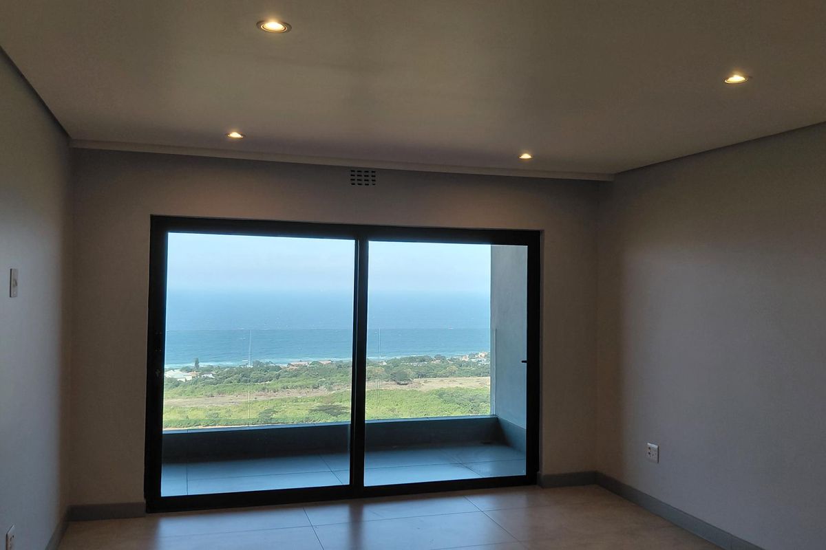An empty living room featuring large sliding glass doors that open to a balcony with expansive ocean and coastal views.