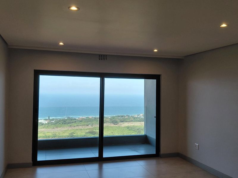 An empty living room featuring large sliding glass doors that open to a balcony with expansive ocean and coastal views.