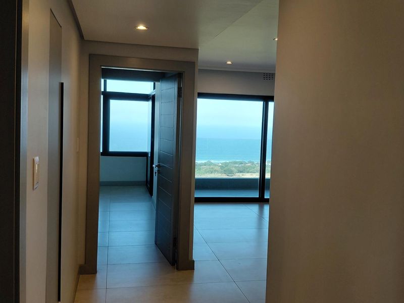 A bright, modern hallway with tiled flooring and recessed lighting, leading into an open-plan living area with expansive ocean views.