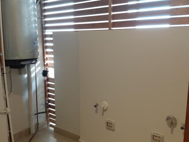 A functional laundry area featuring a wall-mounted electric water heater, dedicated plumbing connections for appliances, and a timber slat privacy screen.