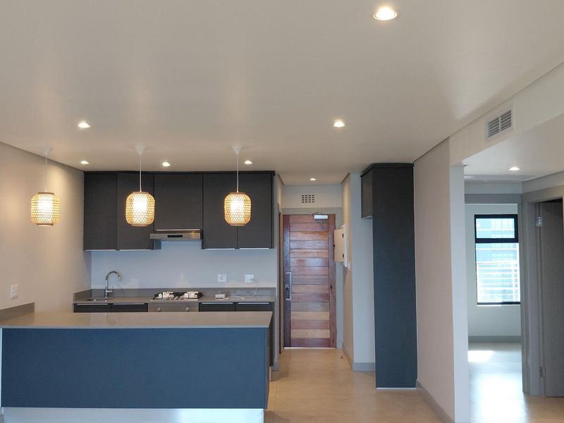 Modern open-plan kitchen featuring dark cabinetry, stone countertops, integrated gas hob, and recessed lighting, flowing into the main living area.