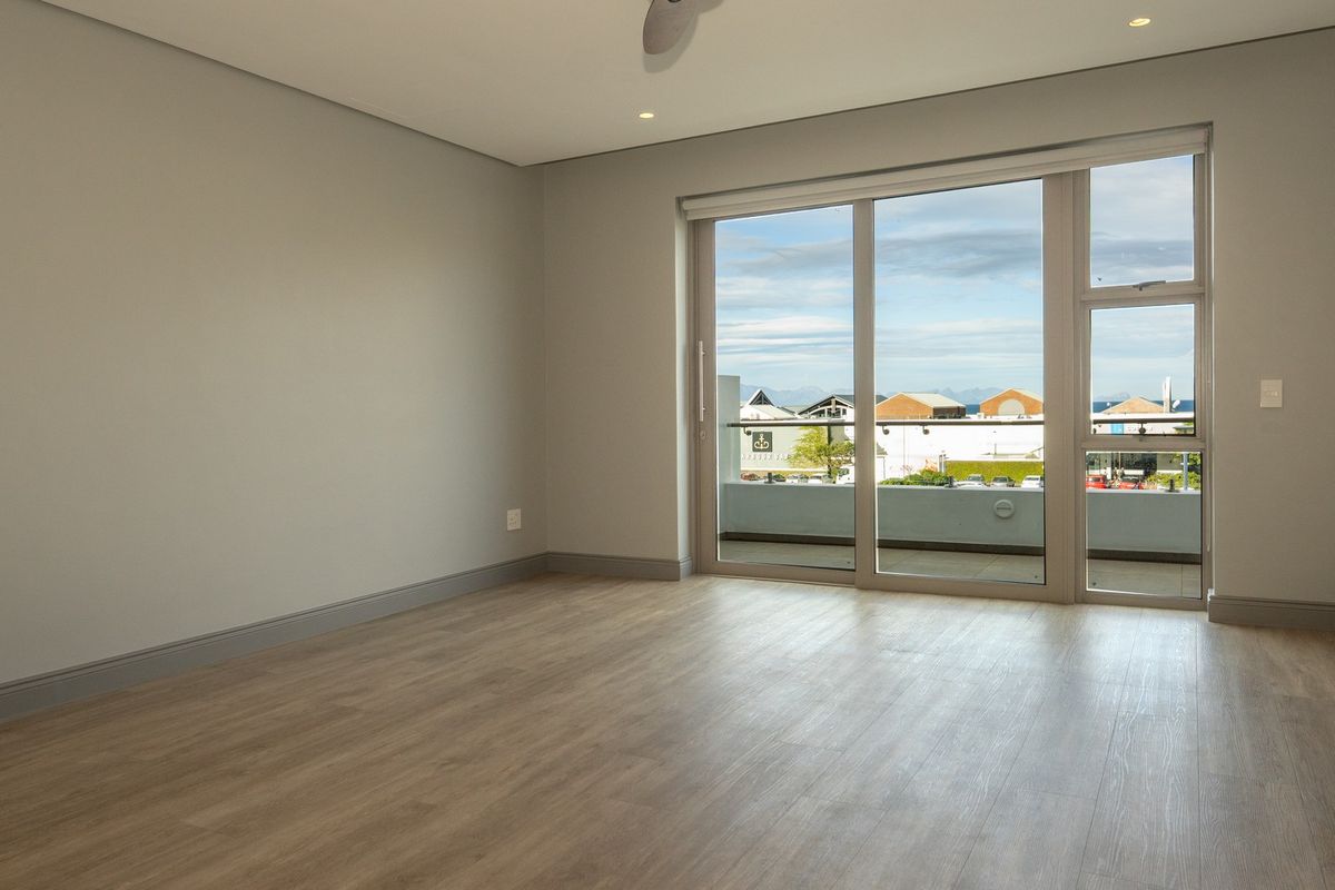 A bright, empty living room featuring modern laminate flooring, recessed lighting, a ceiling fan, and large sliding glass doors leading to a balcony.